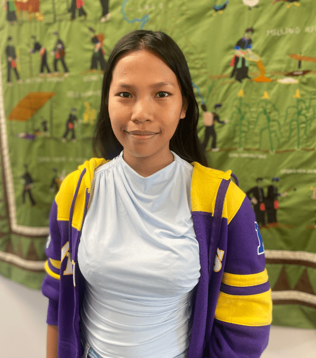 A New American woman in a purple and yellow sweatshirt smiles at the camera.