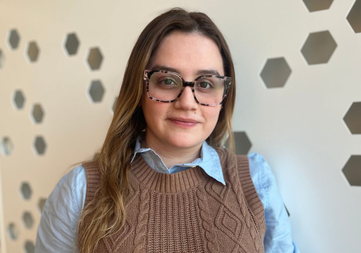 A woman with long brown hair and glasses wearing a blue shirt and brown sweater vest