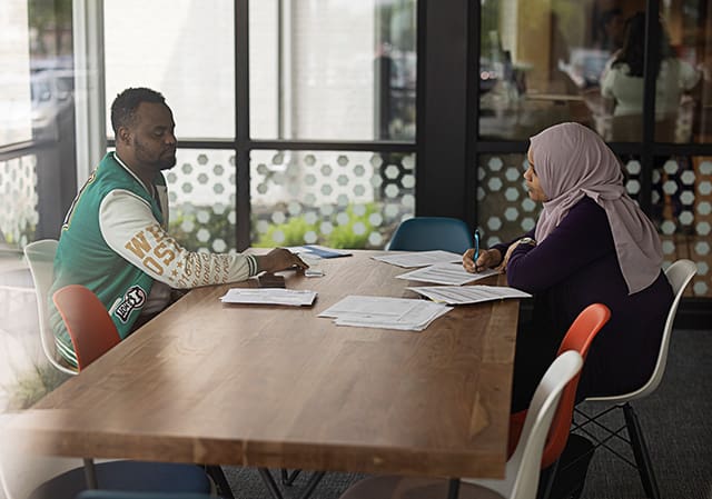 A woman meets with a male refugee who sits across from her at a desk.