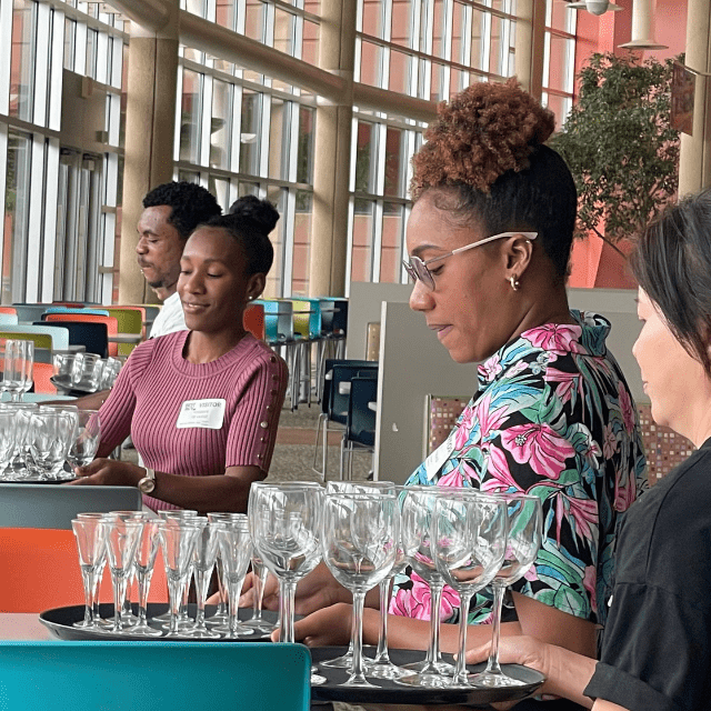 New Americans hold trays of drinking glasses while in job training.
